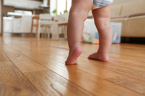 Baby boy doing his frst steps on the living room hardwood floor barefoot.