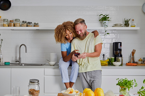 A romantic multiracial couple in the kitchen, enjoying in a happy moment while purchasing groceries online using digital payment, image with a large copy space area