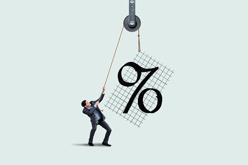 A man uses a hoist and a rope to lift interest rates.