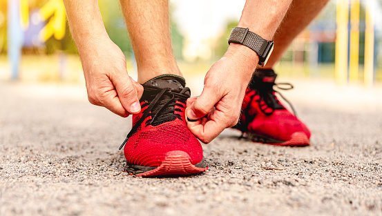 Man tying shoelace on red sneakers during street workout, close up view