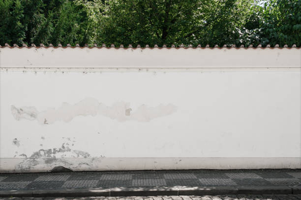 Long old concrete wall covered with white plaster at city street.