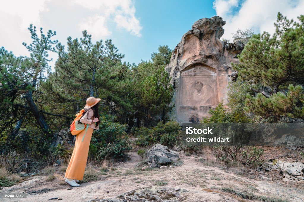 Beautiful traveler girl is watching the small Midas monument , Yazilikaya in the Phrygian valley in Phrygia ,Turkey frig valley, frigler, frigya, Phrygians,  Phrygia, frig vadisi 30-34 Years Stock Photo