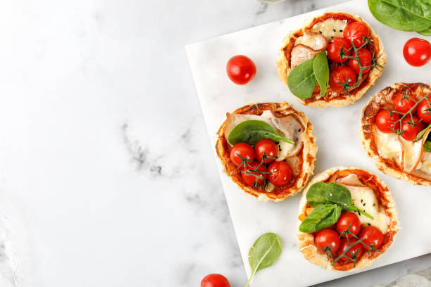 istock Mini Pizzas with tomatoes, cheese and ham. Small homemade pizza, open pie on marble board and white background. 1428817593