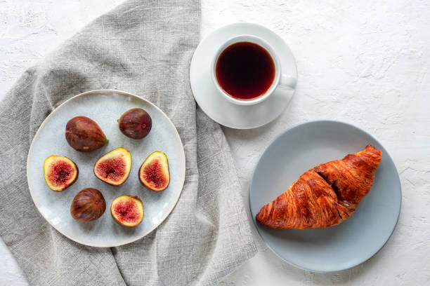 Healthy breakfast with coffee cup, croissant and figs on white textured table. Top view, flat lay