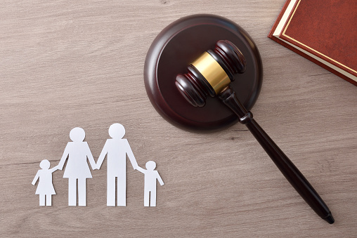 Family and minor judicial protection concept with judge's gavel and law book on a wooden table and family cutout. Top view