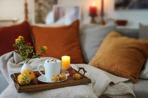 Relaxation with hot chocolate on a tray with candles and autumn decoration on the couch in a cozy living room, copy space, selected focus, narrow depth of field