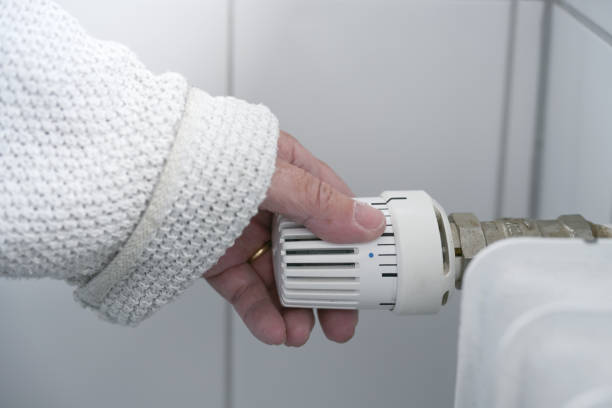 Hand of a woman in warm clothes reduces the heat at the thermostat on the radiator due to the energy crisis with rising prices, copy space, selected focus stock photo