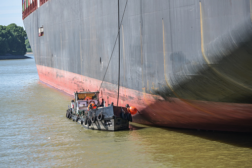 Tanker boat or bunker barge at the hull of a large container freighter takes over oily residues and sanitary wastewater in the cargo port of Hamburg, Germany, copy space, selected focus