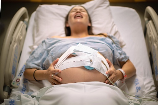 Smiling pregnant woman in hospital bed holding big belly with hands