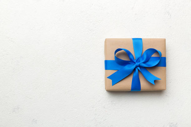 Holiday gift box wrapped in craft paper with colored bow on table background. Top view, flat lay, copy space