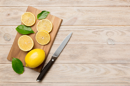 Top view with copy space for fresh and ripe lemons on cutting board. Healthy food background. Elegant background of lemon and lemon slices with squeezer and knife colored background.