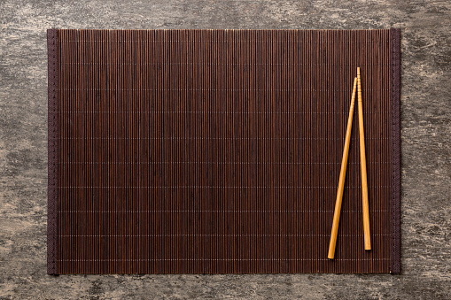 Two chopsticks and bamboo mat on cement background. Top view, copy space.