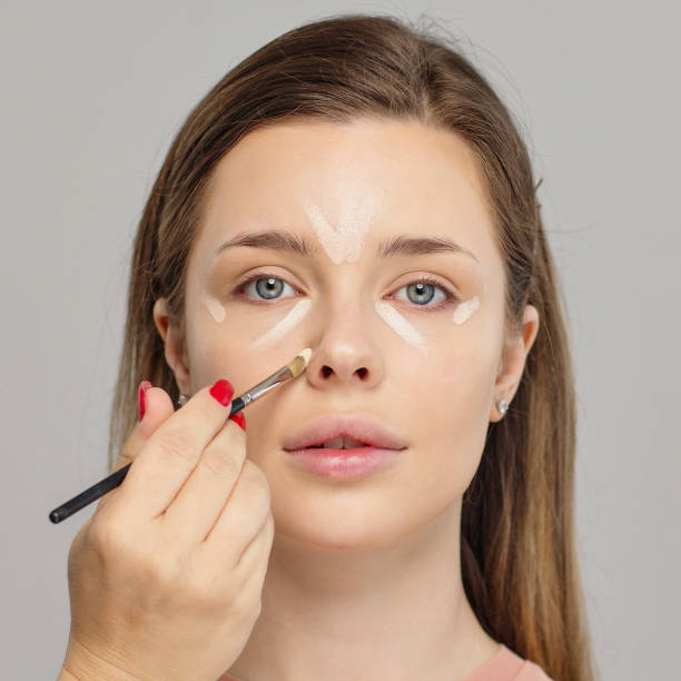 Makeup artist or stylist applies foundation or concealer to the face of the female model. Visagiste  applying cosmetic foundation base on a face. Professional makeup. Tutorial makeup. stock photo