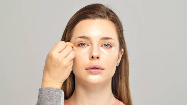 Makeup artist or stylist applies foundation using wet sponge to the face of the female model. Visagiste  applying cosmetic concealer base on a face. stock photo