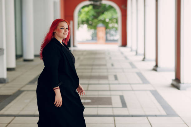 mujer europea de talla grande caminando por la ciudad de la calle al aire libre. joven chica de cabello rojo rosa positivo - teen obesity fotografías e imágenes de stock