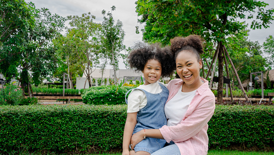 Happy african american woman and daughter pointing a finger showing to something in the park.mother and daughter hug in a park. Happy mother and daughter in the spring park. Beauty nature scene.