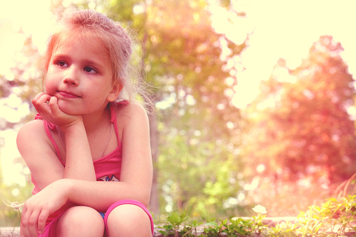 Pensive toddler girl with brown hair and blue eyes in a parkland.