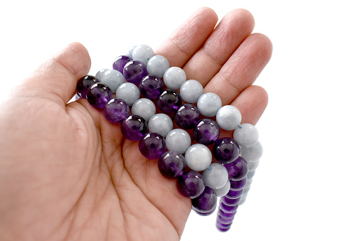 Amethyst and aquamarine bead strands on a woman hand. Crystal gemstones in hand on white background.
