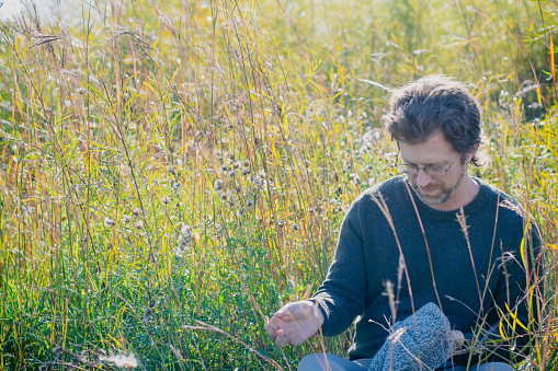 The man is sitting in the tall grass at the assiniboine forest