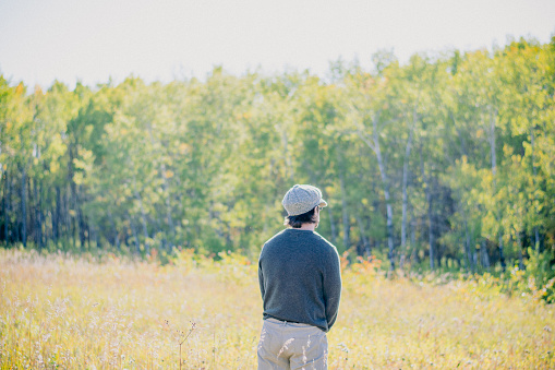 A middle aged man is standing in a field overlooking the  beautiful canadian forest in autumn
