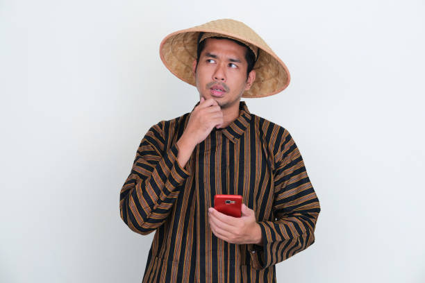 Indonesian traditional farmer thinking about something while holding mobile phone