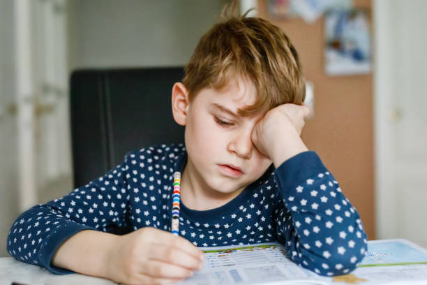 Hard-working sad school kid boy making homework. Upset tired child on home schooling, learning. stock photo