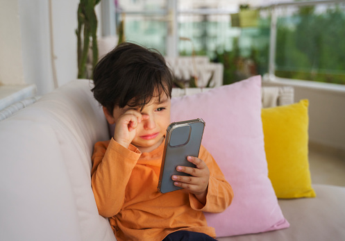 Cute little boy crying because he doesn't want to give the phone back, close up portrait