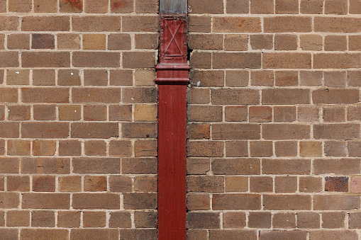 Old brown metal water pipe down a brick wall.