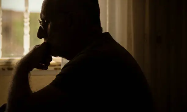 Sideview of adult man with glasses using laptop in room