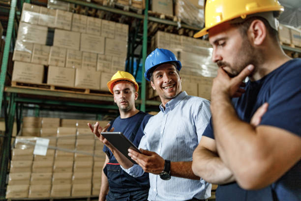 istock Happy inspector using digital tablet and talking to warehouse workers in a storage room. 1428935911