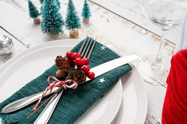 istock Christmas table setting with white dishware, silverware and red and green decorations on white wooden background. High angle view. 1428949742