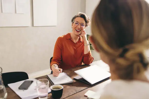 Female hiring manager smiling happily while interviewing a job candidate in her office. Cheerful businesswoman having a meeting with a shortlisted job applicant in a modern workplace.