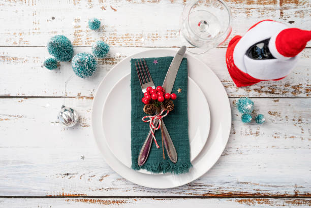 istock Christmas table setting with white dishware, silverware and red and green decorations on white wooden background. Top view. 1428953319