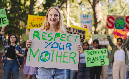 Cheerful teenager smiling at the camera while leading a march against global warming. Group of multiethnic youth activists protesting against climate change. Teenagers joining the global climate strike.