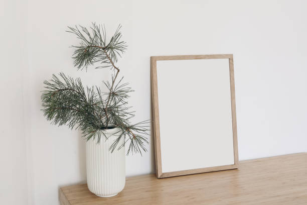 istock Christmas Scandinavian interior. Minimal winter artistic composition. Blank vertical wooden picture frame mockup. Pine tree branches in vase on table, desk. Beige wall background. Empty copy space. 1428954588