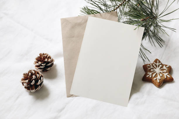 Christmas still life. Empty greeting card, invitation mockup. Gingerbread cookie, pine cones and pine tree branches on white linen tablecloth in sunlight. Gift wrapping concept. Winter festive flatlay stock photo