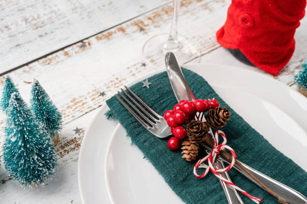 istock Christmas table setting with white dishware, silverware and red and green decorations on white wooden background. High angle view. 1428955524