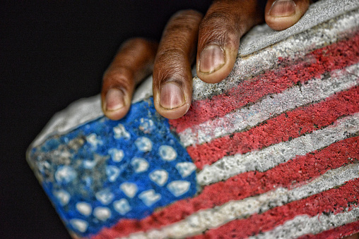 African American Male holding a brick with the American flag painted on it.