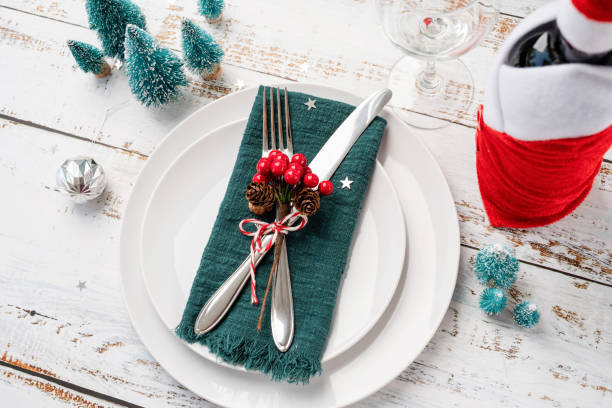 istock Christmas table setting with white dishware, silverware and red and green decorations on white wooden background. High angle view. 1428955753