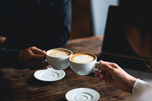 Primer plano de un hombre y una mujer tintineando una taza de café blanco en una cafetería. mientras habla en el trabajo photo