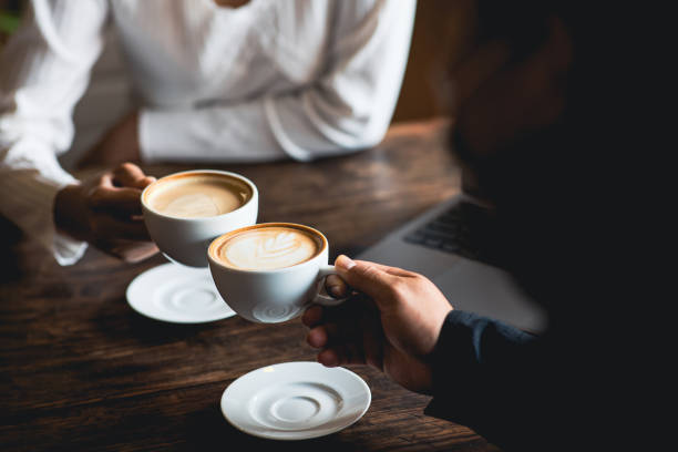 コーヒーショップで白いコーヒーカップを鳴らす男女のクローズアップ。職場での会話中 - toast women white horizontal ストックフォトと画像