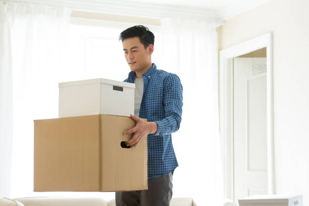 Young man carrying a stack of moving cardboard boxes in a home room - stock photo stock photo