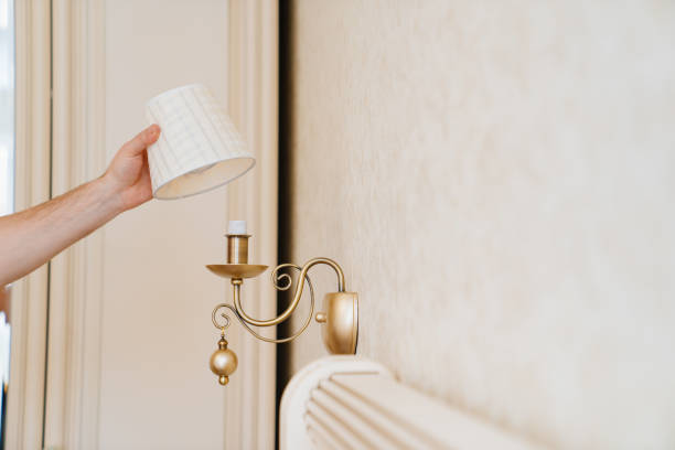 A male electrician changes the light bulbs and repairs in the sconces