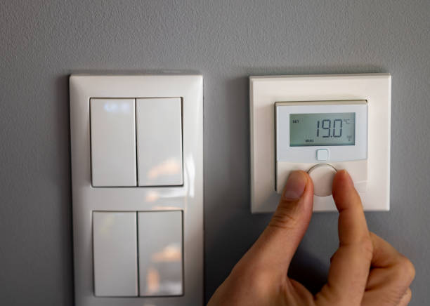 Hand turns down the temperature to 19 degrees Celsius on a electronic thermostat. Symbol for saving energy. stock photo