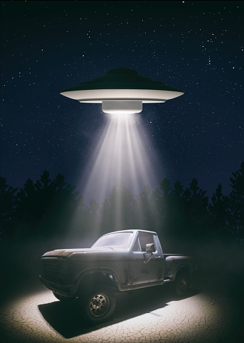 An old-style UFO hovers over a beaten-up pick-up truck on a deserted road, with a beam of intense light from the spaceship probing the truck's cab. Miniature photography.