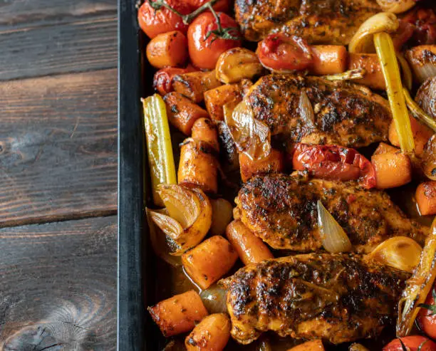 Delicious and homemade cooked low carb dinner or lunch with roasted chicken breast and mediterranean vegetables. Served ready to eat on a baking tray isolates on wooden table. Top view with copy space