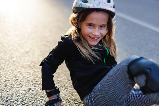 Smiling little girl looking at camera after fell down with roller skates