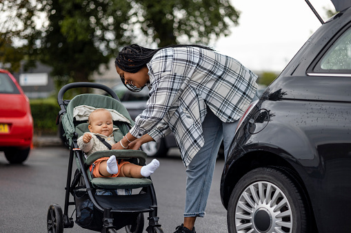 Woman strapping her baby into a stroller beside her car after arriving at a supermarket in the North East of England.