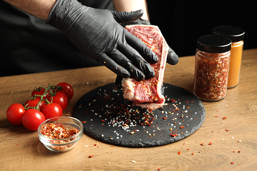 The chef rubs a beef steak with spices.