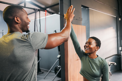 Fitness, personal trainer and a black woman high five man for gym goal achievement. Motivation, workout and a happy couple training together. Health, wellness and exercise support for sports friends.